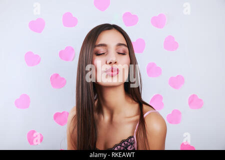 Carino bella bruna giovane donna in piedi e invio di kiss su sfondo grigio con Cuori rosa Foto Stock