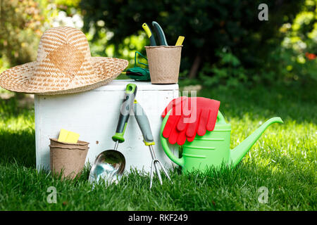 Attrezzi per giardinaggio, guanti, cappello di paglia e legno bianco sulla scatola verde erba, la manutenzione del giardino e il concetto di hobby Foto Stock