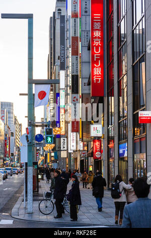 Tokyo, Ginza, ora d'oro. Visualizzare lungo il marciapiede, alto luogo memorizza e verticale negozio illuminati segni sul lato di coda del traffico lungo la strada su altri. Foto Stock