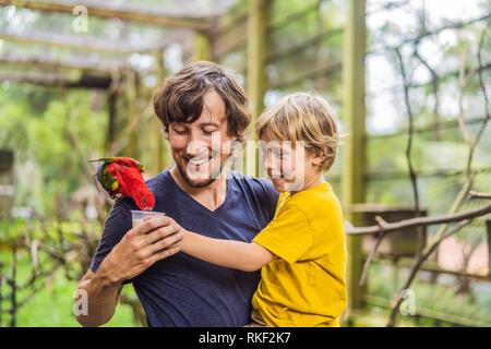 Ded e figlio di alimentare il pappagallo nel parco. Trascorrere il tempo con i bambini del concetto. Foto Stock