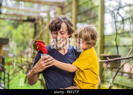 Ded e figlio di alimentare il pappagallo nel parco. Trascorrere il tempo con i bambini del concetto. Foto Stock