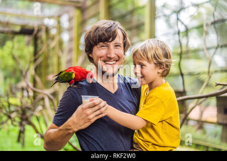 Ded e figlio di alimentare il pappagallo nel parco. Trascorrere il tempo con i bambini del concetto. Foto Stock