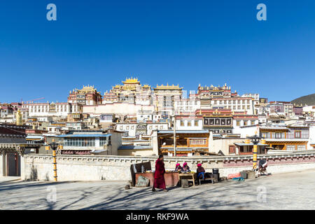 Monaco buddista passando accanto ai venditori locali in Ganden Sumtseling o monastero Songzanlin, Shangri La, nella provincia dello Yunnan in Cina Foto Stock