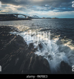 Costa rocciosa dall'Oceano Atlantico strada in Norvegia. Scatti con lunghi tempi di esposizione. Vista sul famoso ponte Storseisundbrua e le onde che si infrangono. Foto Stock