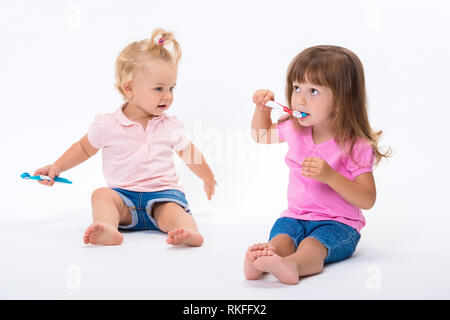 Due ragazze sorelle in t-shirt rosa con gli spazzolini da denti di stand per la loro altezza piena isolati su sfondo bianco. Bambini l'igiene orale e dentale. Foto Stock