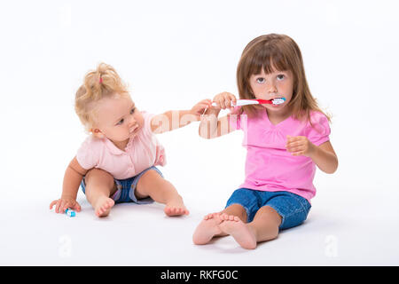 Due ragazze sorelle in t-shirt rosa con gli spazzolini da denti di stand per la loro altezza piena isolati su sfondo bianco. Bambini l'igiene orale e dentale. Foto Stock