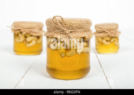 Noci di acagiù con miele in vasetti di vetro su bianco di tavole di legno. Delizioso dolce leccornia. Foto Stock