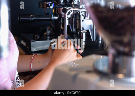 Donna asiatica Barista azienda brocca e controlla la temperatura per la preparazione di schiuma di latte per il cappuccino o latte caffè Foto Stock