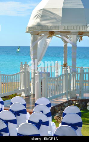 Matrimonio bianco gazebo in un mare di giardino tropicale a destinazione di un ricevimento di matrimonio con sedie decorate schierate per una cerimonia civile. Foto Stock