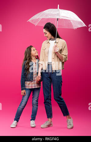 Felice la figlia e la madre con ombrello tenendo le mani e sorridente ogni altra in rosa Foto Stock