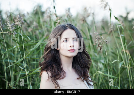 Bella donna pensieroso outdoors su foglie verdi e lo sfondo di erba nel parco di primavera Foto Stock