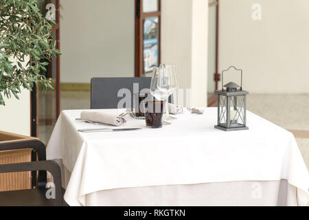 Una tabella vuota per due in un ristorante, coperto con una tovaglia bianca con due set di tavolo e una lanterna, in un bar o un ristorante esterno. Foto Stock