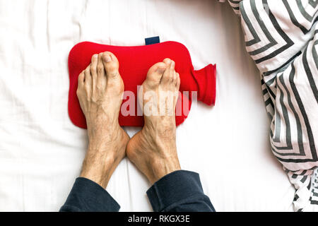 Uomo con i piedi freddi a letto su un red hot acqua in bottiglia. Il riscaldamento dei piedi freddi Foto Stock