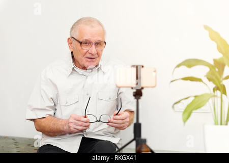 Sorridente eldery uomo guardando la telecamera rendendo il video blog o chiamare a casa seduti sul divano dating online headshot ritratto Foto Stock