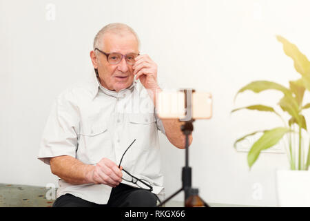 Sorridente eldery uomo guardando la telecamera rendendo il video blog o chiamare a casa seduti sul divano dating online headshot ritratto Foto Stock