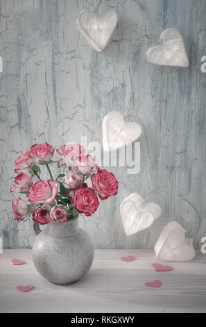 Il giorno di San Valentino ancora in vita con carta bianca card, le rose rosa e ghirlanda di luci in forma di cuori di carta su sfondo rustico Foto Stock