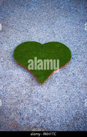 Un intaglio Cuore in plastica verde erba a bordo si trova su una strada di ghiaia Foto Stock