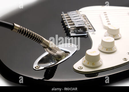 Parte della moderna electric six string guitar colore nero con finitura lucida con jack di metallo nel socket, ritiri e le manopole di comando isolato su bianco backgr Foto Stock