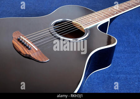 Classic acoustic sei corde della chitarra di colore nero con la parte superiore in spaccato frammento su sfondo jeans vista laterale vista dettagliata Foto Stock