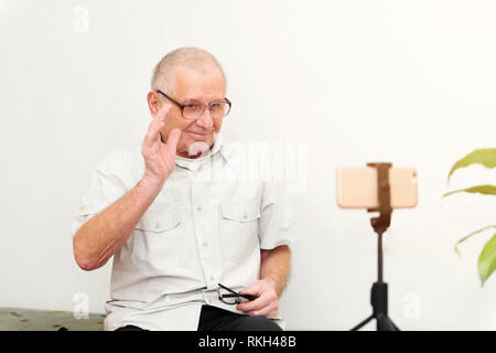 Sorridente eldery uomo guardando la telecamera rendendo il video blog o chiamare a casa seduti sul divano dating online headshot ritratto Foto Stock