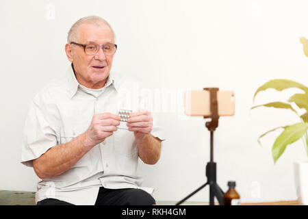 Sorridente eldery uomo guardando la telecamera rendendo il video blog o chiamare a casa seduti sul divano dating online headshot ritratto Foto Stock