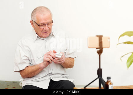 Sorridente eldery uomo guardando la telecamera rendendo il video blog o chiamare a casa seduti sul divano dating online headshot ritratto Foto Stock