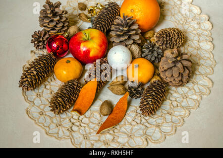 Tovagliolo ricamato con regali per Natale da apple, tangerini, noci, mandorle, giocattoli di Natale con diversi coni di conifere su legno compensato Foto Stock