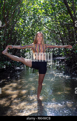 Giovane donna a praticare yoga (Extended mano-a-Big-Toe pongono - Utthita Hasta Padangustasana) in un ambiente naturale - Fort Lauderdale, Florida, Stati Uniti d'America Foto Stock