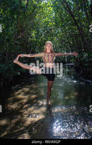 Giovane donna a praticare yoga (Extended mano-a-Big-Toe pongono - Utthita Hasta Padangustasana) in un ambiente naturale - Fort Lauderdale, Florida, Stati Uniti d'America Foto Stock