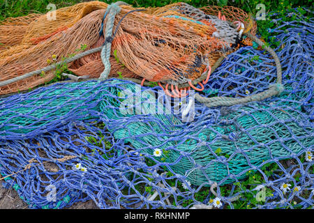 Arancio e blu colorato reti da pesca giacente su erba e fiori spiata attraverso. Entrambi sono invecchiati e sbiadita, scartata. daylight immagine sul giorno grigio. Foto Stock