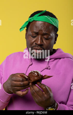 Sconvolto persona maschio fissando cupcake al cioccolato Foto Stock