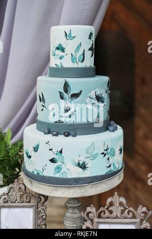 Bella blu tre-tiered torta decorata con fiori su un cavalletto, sul tavolo di nozze. Foto Stock