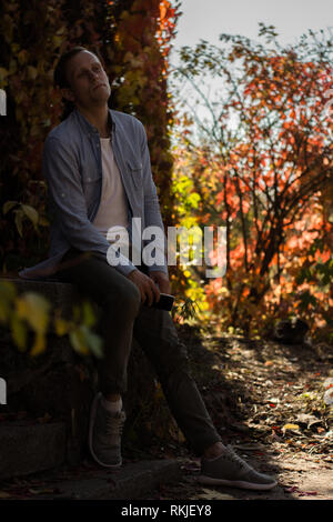 Triste ragazzo con telefono in abiti casual in autunno park Foto Stock