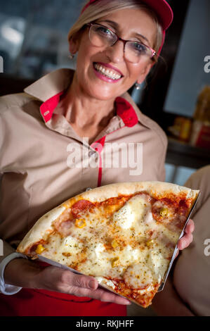 Lo chef femmina in posa con un trancio di pizza in un ristorante fast food. Cucina italiana fast food Foto Stock