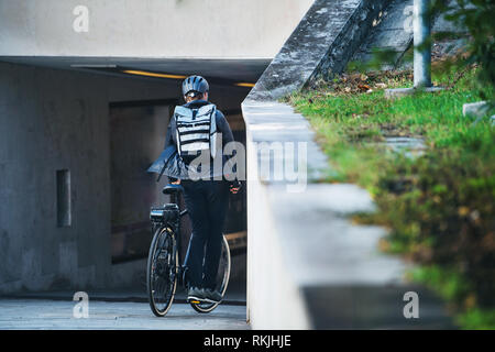 Una vista posteriore della bicicletta maschio corriere consegna di pacchi in città. Copia dello spazio. Foto Stock