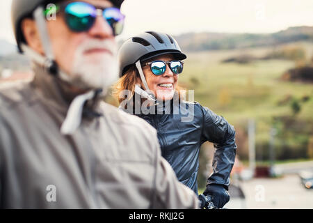 Attivo coppia senior con electrobikes in piedi all'aperto su una strada in natura. Foto Stock