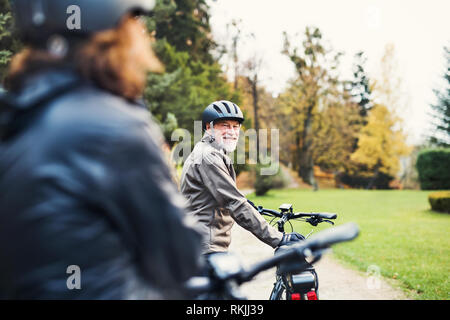 Attivo coppia senior con electrobikes in piedi all'aperto su una strada in natura. Foto Stock