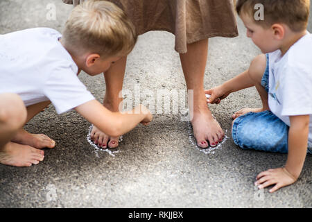 Due piccoli figli giocare con la madre su una strada nel parco in un giorno d'estate. Foto Stock