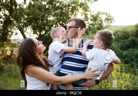 Una giovane famiglia con due figli piccoli in piedi all'aperto in natura in un giorno di estate. Foto Stock