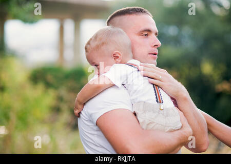 Giovane padre tenendo un piccolo pianto toddler figlio nella soleggiata estate natura. Foto Stock
