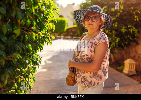 Felice donna senior camminando sul territorio di hotel. La vacanza estiva. Elegante look alla moda Foto Stock