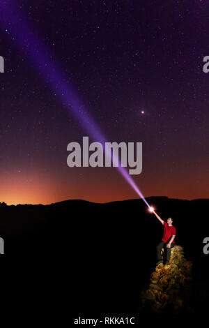 Un uomo seduto rivolto a un cielo stellato con una torcia. Foto Stock