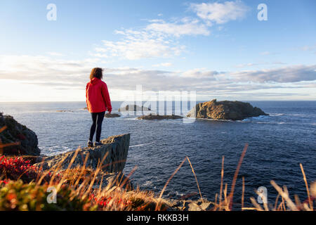 Woman in Red jacket è in piedi sul bordo di una scogliera godendovi lo splendido paesaggio dell'oceano. Preso in testa di corvo, Nord Twillingate Isola, Newfoundlan Foto Stock