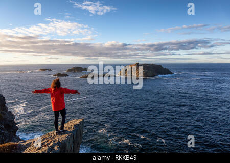 Woman in Red jacket è in piedi sul bordo di una scogliera con le braccia aperte e godere degli splendidi paesaggi dell'oceano. Preso in testa di corvo, Nord Twillingate Foto Stock