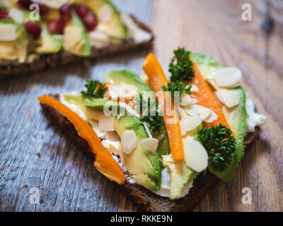 Delizioso e sano avocado toast con melograno, peperone e mandorla rustico di legno Foto Stock