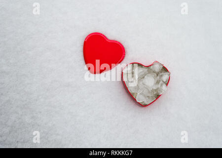 Un cuore rosso scatola sagomata con ghiaccio cubs interno e copiare lo spazio per il tuo testo. Il cuore rosso a forma di coperchio accanto alla casella, mezzo sepolto in uno strato di neve. Va Foto Stock