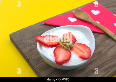 La fragola e yogurt snack accompagnati da un tovagliolo decorato con cuori e cucchiaio di legno su legno tabella vintage Foto Stock
