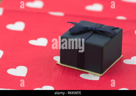 Confezione regalo decorata con un fiocco blu e bianco cuori su sfondo rosso Foto Stock