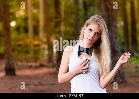 Bella ragazza bionda nel parco al tramonto mobile di contenimento vicino al petto - Immagine Foto Stock