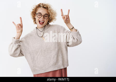 Yeah questo partito rocce. Spensierato giocoso e upbeat donna che indossa il vestito elegante e bicchieri chiudere gli occhi dalla gioia godendo fantastico party mostra rock-n Foto Stock